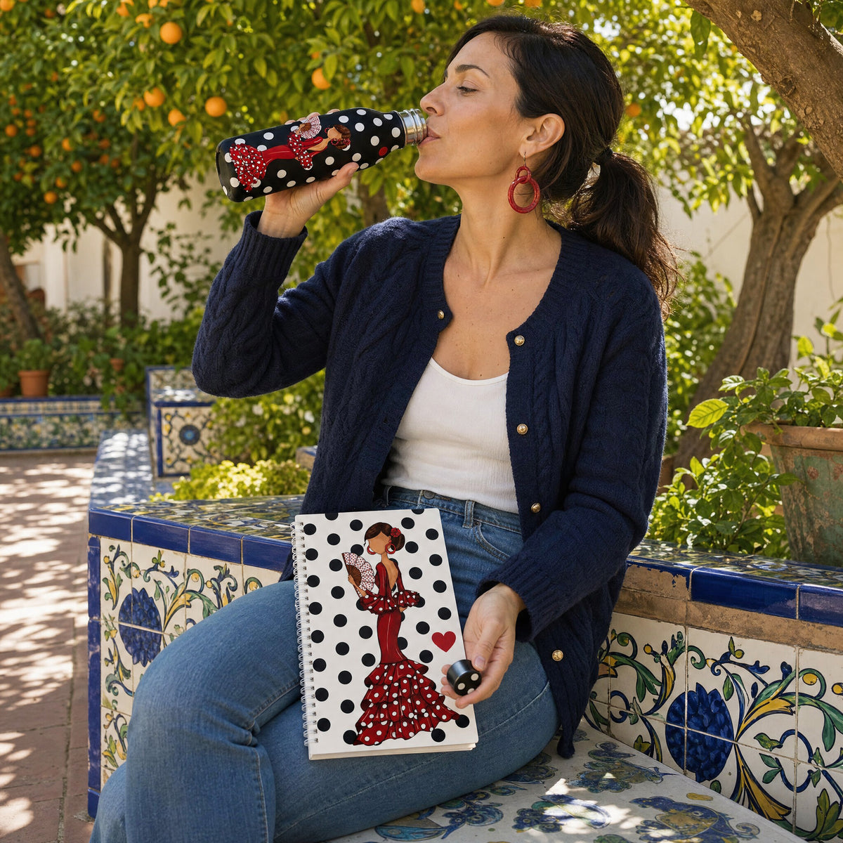 Mujer bebiendo de la botella térmica flamenca Pepa con la libreta a juego en el regazo