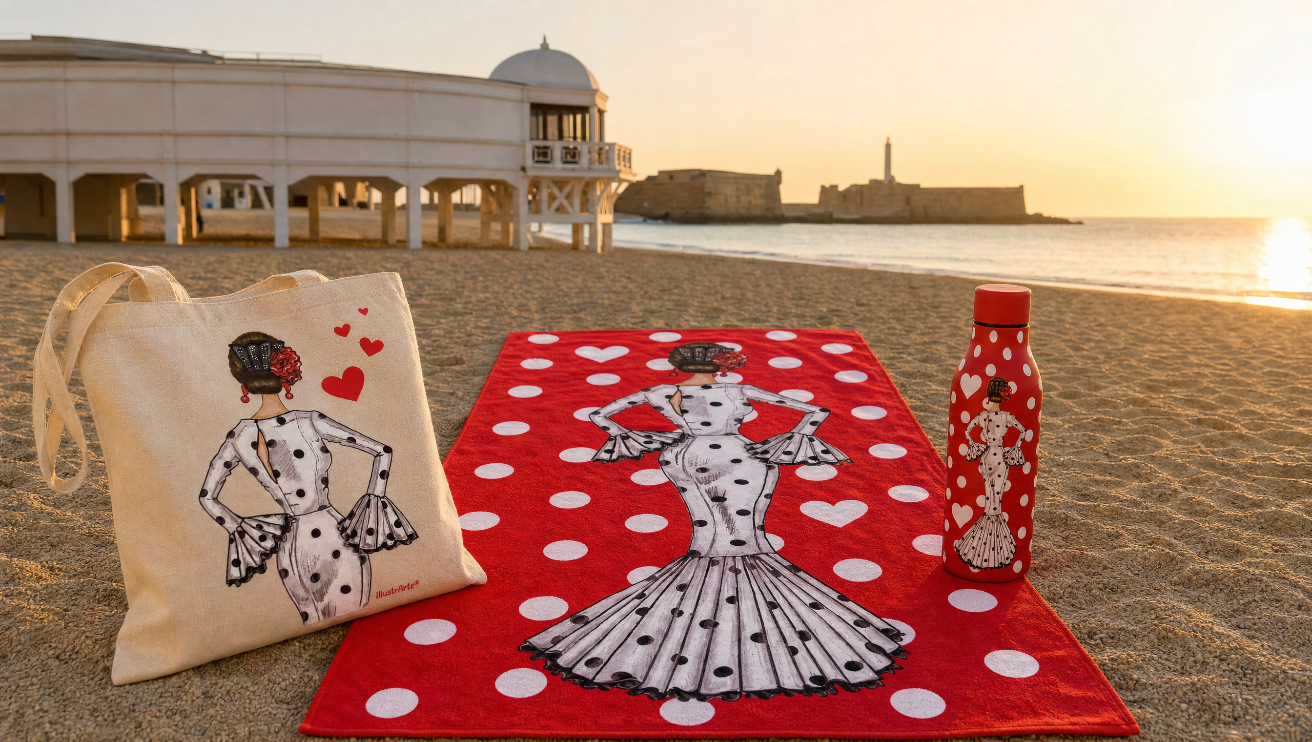 Bolsa tote, toalla de playa y botella térmica flamencas de illustrArte sobre la arena de La Caleta, Cádiz, con el Balneario de la Palma y el Castillo de San Sebastián al fondo