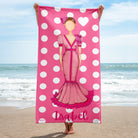 una mujer de pie en una playa sosteniendo una toalla rosa con la imagen de una mujer